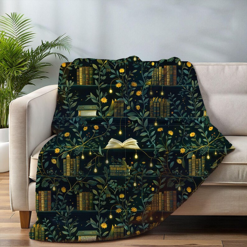 May include: A dark blue throw blanket featuring a repeating pattern of bookshelves, books, and floral elements. The design includes yellow flowers and string lights, creating a cosy, whimsical aesthetic. The blanket is draped over a beige sofa.