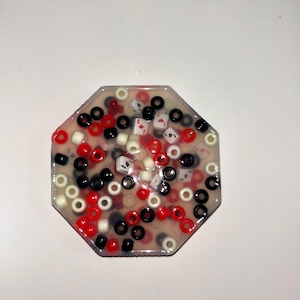 Può includere: Un sottobicchiere in resina ottagonale trasparente con perline rosse, bianche e nere e simboli di carte da gioco incorporati.