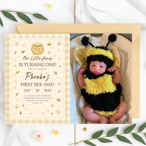 May include: A baby dressed in a yellow and black bee costume, with a matching hat, is featured on a birthday invitation. The invitation has a bee theme with the text "Our Little Honey is Turning One!" and "Phoebe's First Bee-Day!"