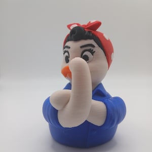 Peut inclure: Figurine imprimée en 3D d'une femme en chemise bleue et foulard rouge à pois, le bras fléchi. La figurine a un visage blanc, des cheveux noirs et un bec orange. L'objet est un article de fantaisie.