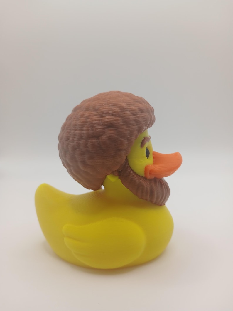 May include: A yellow rubber duck with a brown wig and beard. The duck has an orange beak and black eyes. The duck is a novelty item, likely for bath time or decoration.
