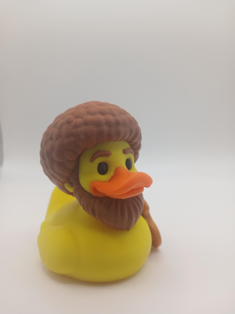 May include: A yellow rubber duck with a brown beard, hair, and a walking stick. The duck has an orange beak and black eyes. The duck is a novelty item.