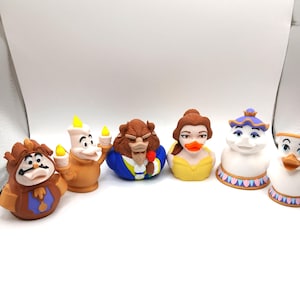 May include: A set of six rubber duck toys, each representing characters from the animated film "Beauty and the Beast." The characters include Cogsworth, Lumiere, Beast, Belle, Mrs. Potts, and Chip. The toys are brightly coloured and detailed.