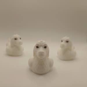 May include: Three white rubber duck toys shaped like dogs with long floppy ears and dark brown eyes. Each toy features a smooth matte finish and a molded canine facial structure, arranged in a triangular formation against a plain white background.