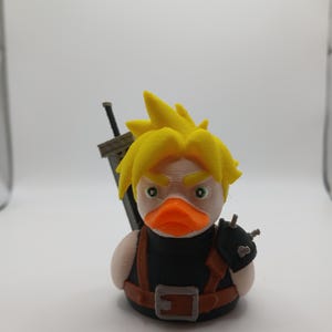 May include: A 3D-printed duck figurine with yellow hair, green eyes, and an orange beak, dressed as a character with a black outfit and a large sword on its back. The duck has a brown belt and shoulder straps.