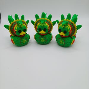 Könnte beinhalten: Drei grüne Entenfiguren mit gelben Schnäbeln und schwarzen Augen. Jede Ente hat einen dekorativen Kopfschmuck mit roten und gelben Akzenten. Die Enten sind in einer Reihe angeordnet und zeigen ihr detailliertes Design und ihre leuchtenden Farben.