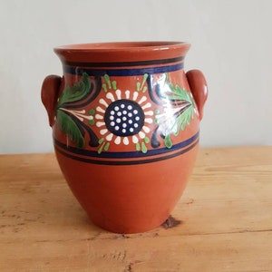 Könnte beinhalten: Ein Terrakotta-Topf mit zwei Henkeln, verziert mit einem floralen Design in Grün, Blau, Weiß und Schwarz.