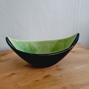 Puede incluir: Un cuenco de vidrio negro y verde con forma de hoja. El cuenco tiene un acabado brillante y un patrón geométrico.