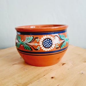May include: A terracotta pot with a blue, white, and green floral design. The pot is glazed and has a rounded shape.