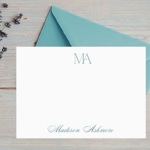 May include: A white stationery set with a teal envelope and a sprig of lavender. The stationery features the initials "MA" at the top and the name "Madison Ashmore" at the bottom, both in teal.