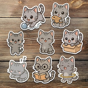 May include: A collection of eight gray cat stickers in various poses. One cat plays with yarn, another holds a fish, and others are in a box, reading, or using a hula hoop. The stickers have a cartoon style with happy expressions.