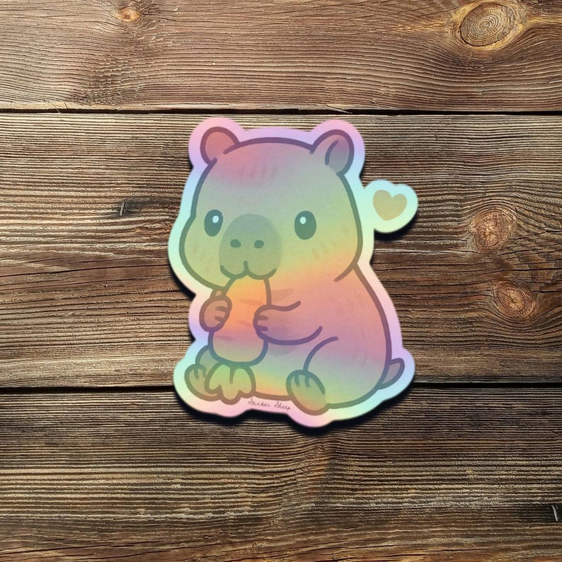 May include: A colorful sticker featuring a cartoon wombat eating a carrot. The wombat is in a rainbow gradient of colors, with a heart-shaped detail. The sticker is on a wooden background.