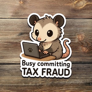 Puede incluir: Una pegatina con un dibujo de una zarigüeya con un portátil. La zarigüeya es gris y marrón con grandes ojos negros y está sentada en un pequeño escritorio. El texto "Busy committing TAX FRAUD" está debajo.