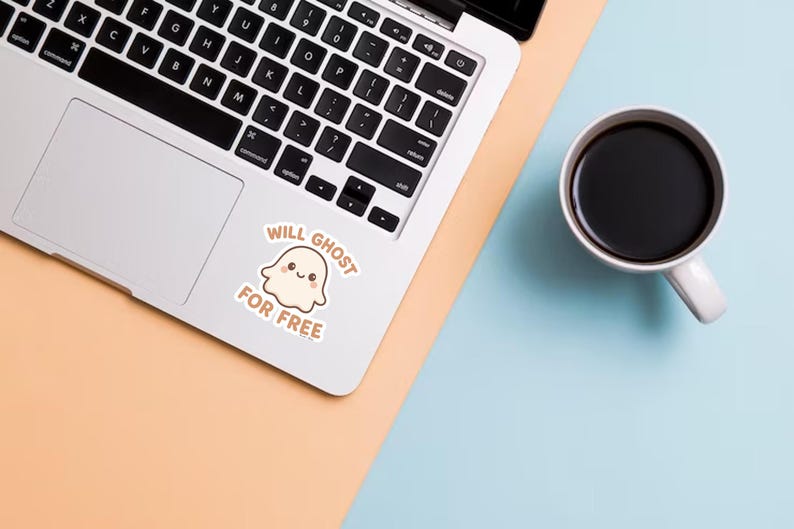 May include: A laptop with a sticker that says "Will Ghost For Free" next to a cup of coffee. The sticker features a cute ghost illustration. The laptop is on a peach and blue surface.