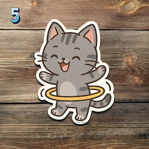 May include: A gray cartoon cat with a yellow hula hoop, smiling and with its arms outstretched. The number 5 is in the upper left corner. The sticker is on a wooden surface.