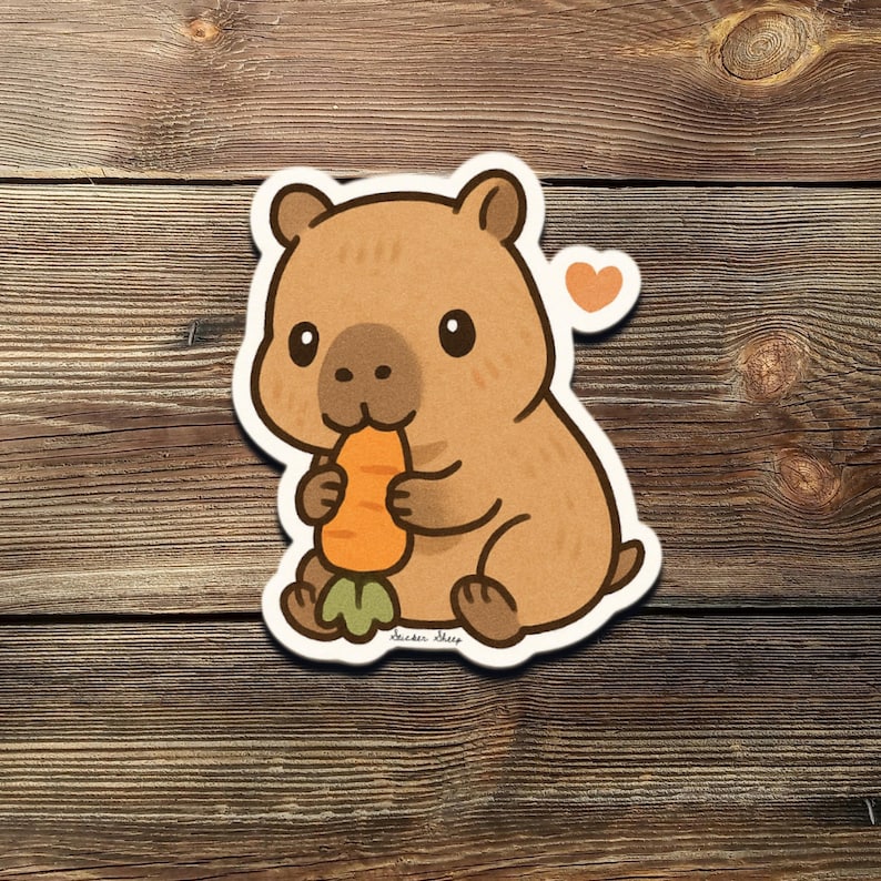 May include: A brown cartoon capybara sticker, eating a carrot. The capybara has a small orange heart above its head. The sticker has a white border and is on a wooden background.