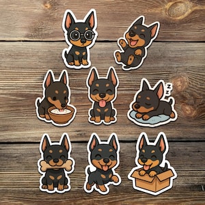 Puede incluir: Colección de pegatinas de estilo caricatura con perros negros y marrones en varias poses. Un perro lleva gafas, otro está durmiendo, y otros están comiendo, jugando o sentados en una caja. Las pegatinas tienen un borde blanco y están sobre un fondo de vetas de madera.