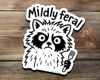 Puede incluir: Pegatina en blanco y negro de un mapache con un tenedor en la mano. El mapache tiene una expresión gruñona y el texto "Mildly feral" está arriba.