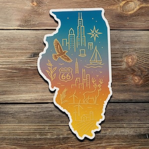 Op de afbeelding: Een sticker in de vorm van Illinois met een verloop van blauw, oranje en geel. Het ontwerp bevat iconische beelden van Illinois, waaronder een vogel, Route 66 en stadsgezichten. De sticker staat op een houten achtergrond.
