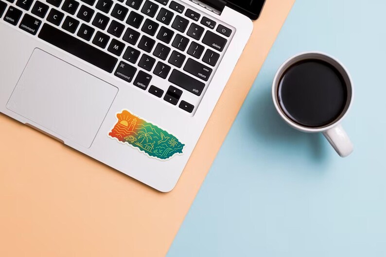 May include: A laptop with a colorful sticker of Puerto Rico, featuring a sunset, palm trees, and ocean waves. A white mug filled with black coffee sits on a light blue surface.