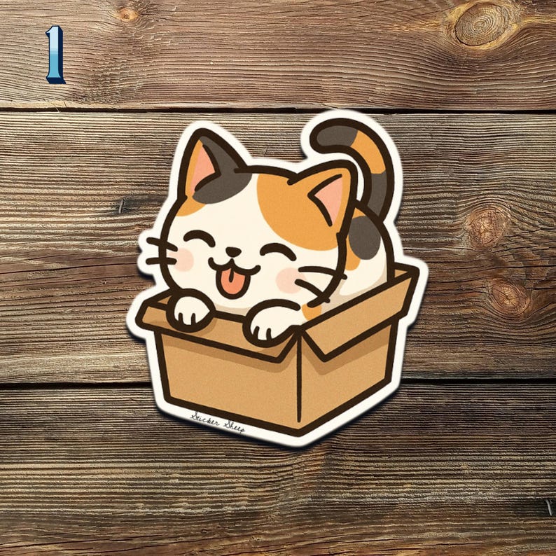 May include: A die-cut sticker featuring a cartoon calico cat with a happy expression, sticking its tongue out while sitting in a cardboard box. The sticker has a white border and is set against a wooden background.