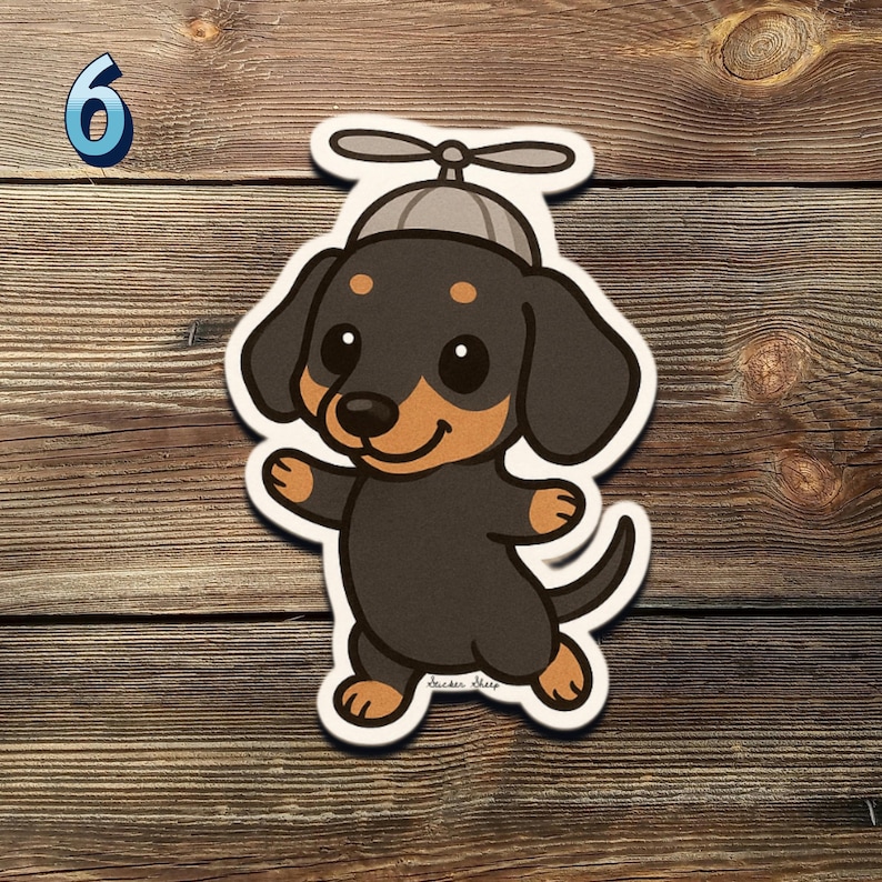 May include: A sticker of a cartoon dachshund dog wearing a propeller hat. The dog is black and tan with a smiling face and outstretched paws. The number 6 is in the upper left corner. The sticker is on a wooden background.