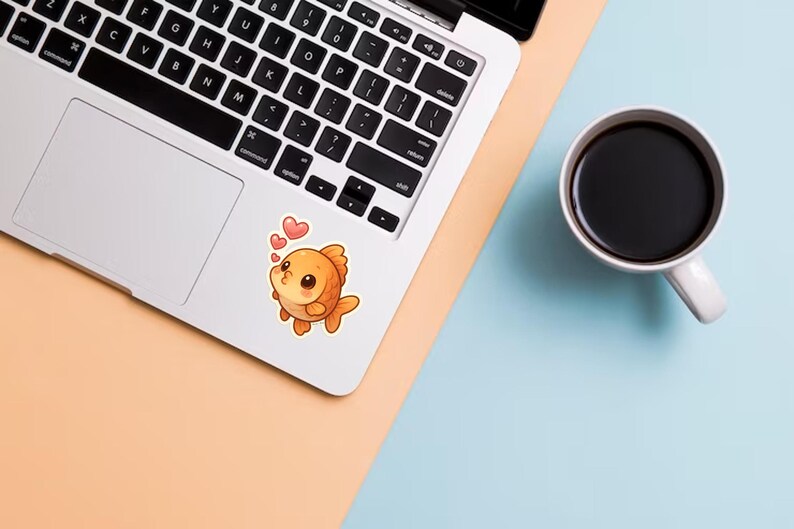 May include: A laptop with a cute orange goldfish sticker blowing kisses, accompanied by two pink hearts. A white mug filled with black coffee sits on a light blue and peach surface.