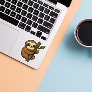 May include: A laptop with a sticker of a cartoon sloth holding a branch with a leaf. A white mug filled with black coffee sits on a light blue and peach surface.