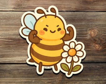 May include: A die-cut sticker featuring a cartoon bee flexing its arms. The bee is yellow and brown with a smiling face and rosy cheeks. A white daisy with a yellow center is next to the bee. The sticker is on a wooden background.