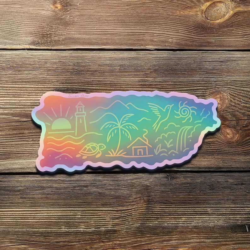 May include: A holographic sticker in the shape of Puerto Rico, featuring a sunrise, lighthouse, palm tree, mountains, a bird, and a turtle. The sticker has a rainbow gradient and is placed on a wooden surface.