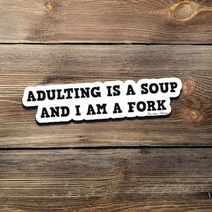 Può includere: Un adesivo bianco con testo nero che recita "ADULTING IS A SOUP AND I AM A FORK." L'adesivo è su uno sfondo di legno.