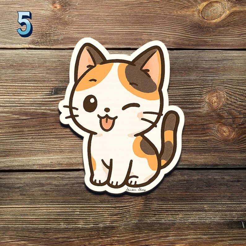 May include: A cartoon sticker of a winking cat with a white body, orange and brown patches, and a brown tail. The cat is sticking out its tongue. The number "5" is in the upper left corner. The sticker is on a wooden surface.