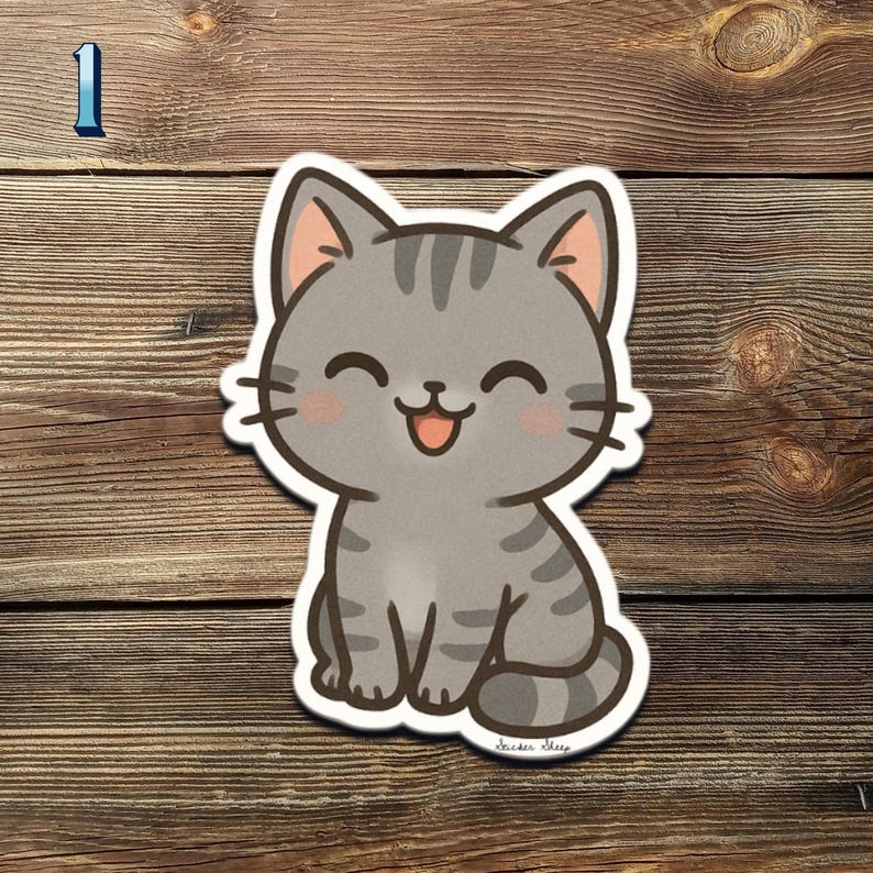 May include: A gray tabby cat sticker with a happy expression. The cartoon cat has pink inner ears and cheeks, with black stripes and whiskers. The sticker is on a wooden surface.