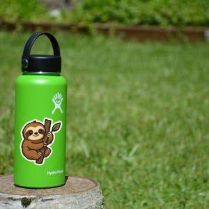 May include: A green insulated water bottle with a black handle and lid. A sticker of a cartoon sloth clinging to a branch is on the bottle. The bottle is sitting on a wooden stump in front of a green grassy background.