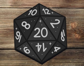 May include: A black, twenty-sided die featuring white numerals and markings. The numbers are arranged around the edges, with the number 20 in the centre. The die is set against a wooden background.