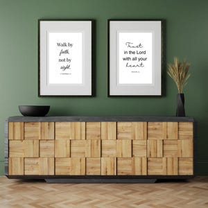 May include: Two framed prints with inspirational quotes. The first print says "Walk by faith, not by sight." The second print says "Trust in the Lord with all your heart." The prints are hanging on a green wall above a wooden cabinet.