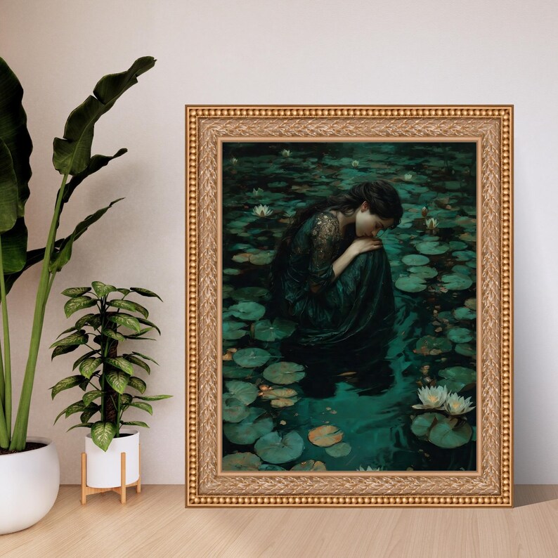 May include: A framed artwork depicts a person in a dark green dress, seated in a pond filled with lily pads and white flowers. The artwork has a gold-colored ornate frame. The person is leaning forward with their head down.