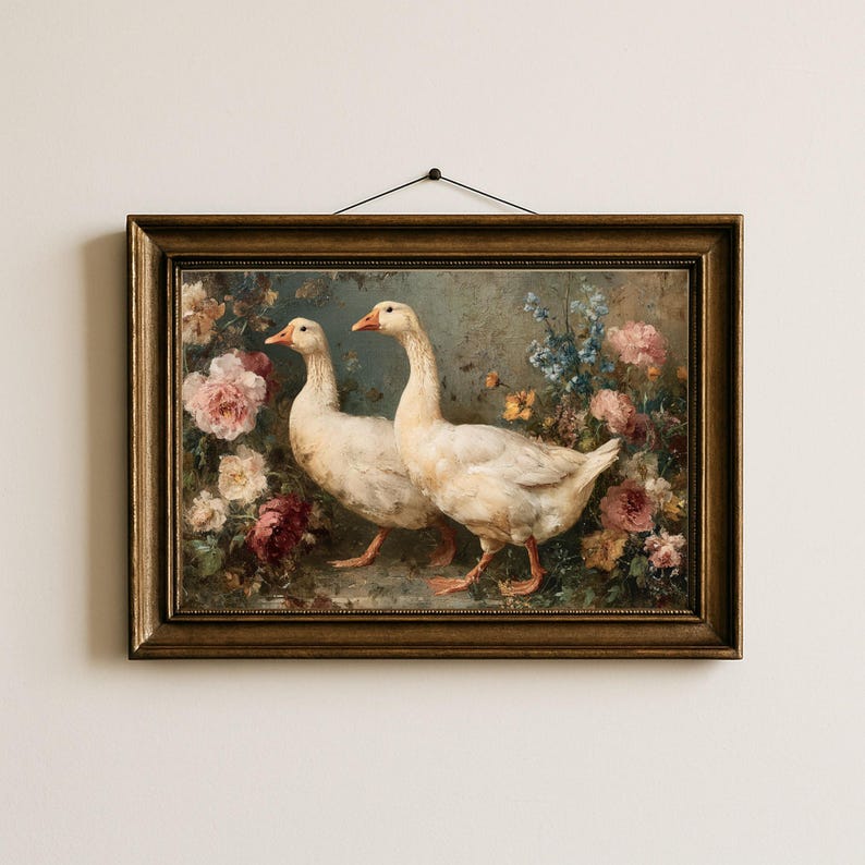 May include: A framed painting featuring two white geese with orange beaks and feet, set against a backdrop of colorful flowers. The artwork is in a gold-toned frame, creating a vintage aesthetic. The painting is hung on a white wall.