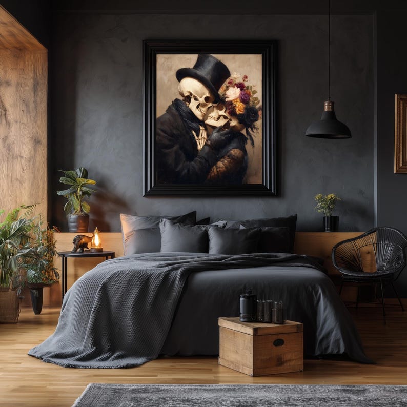 May include: A framed artwork depicts two skeletons embracing, one wearing a top hat and the other adorned with flowers. The artwork hangs above a bed with gray bedding, complemented by a wooden nightstand and a black pendant light.
