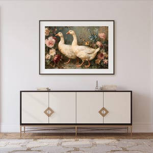 May include: Framed artwork featuring two white geese with orange beaks and feet, set against a backdrop of colorful flowers. The painting is displayed above a white cabinet with gold accents, creating a classic and elegant aesthetic.