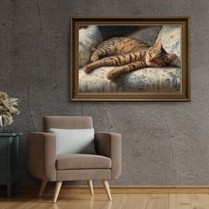 May include: A framed print of a tabby cat resting on a floral patterned cushion. The cat has brown and black stripes and is lying down with its eyes closed. The frame is a warm brown color.