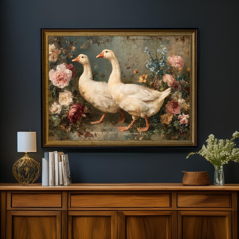 May include: A framed painting depicts two white geese with orange beaks and feet, set against a backdrop of colorful flowers. The artwork is framed in a gold-colored frame and hangs on a dark blue wall.