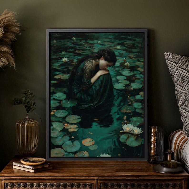 May include: A framed art print depicts a person in a dark green dress, seated in a pond filled with lily pads and white flowers. The artwork has a dark, moody aesthetic, with a focus on the figure's posture and the water's reflections.