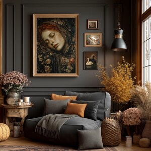 May include: A cozy living room scene with a large framed portrait of a woman with red hair, and several smaller framed paintings. A gray sectional sofa is adorned with orange and gray pillows and a gray throw blanket. Decorative dried flowers and a woven basket add warmth.