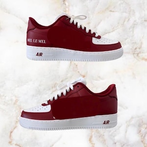 May include: Two pairs of red and white sneakers with white laces. The sneakers have the text "MEL LE-MEL" on the side and "AIR" on the midsole. The shoes are on a white sole.