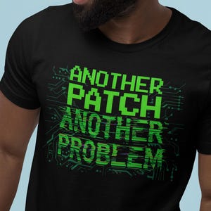 Puede incluir: Camiseta negra con el texto "ANOTHER PATCH ANOTHER PROBLEM" en verde brillante, con fuente pixelada. El texto está dispuesto en tres líneas con un diseño de placa de circuito. La camiseta es de cuello redondo.