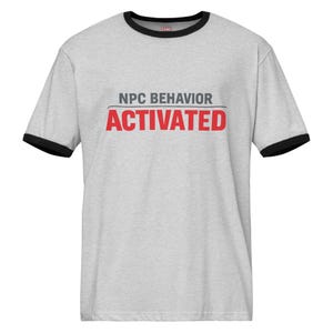 Può includere: T-shirt grigio chiaro con bordi neri su colletto e maniche. Il testo "NPC BEHAVIOR" in grigio è sopra la parola "ACTIVATED" in rosso. Abbigliamento casual.