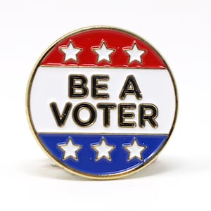 May include: A gold-coloured pin with a red, white and blue design. The pin features five white stars and the text "BE A VOTER" in black letters.
