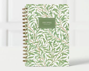 May include: A spiral-bound recipe journal with a green and white botanical pattern. The cover features a rectangular label with the word "RECIPES" and the family name. The journal has a gold spiral binding.