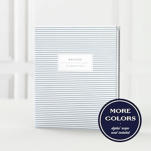 May include: A recipe binder featuring a white cover with thin horizontal blue stripes. A central white rectangular label displays the text RECIPES and THE BEAUMONT FAMILY. A circular dark blue badge in the corner reads MORE COLORS.